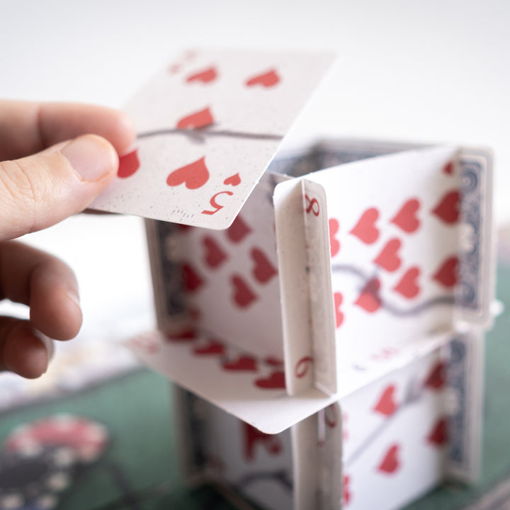 Hand building a card tower with playing cards. Games Night in an envelope and tabletop Escape Room Game. Similar to an Exit Game. Same genre as murder mystery.