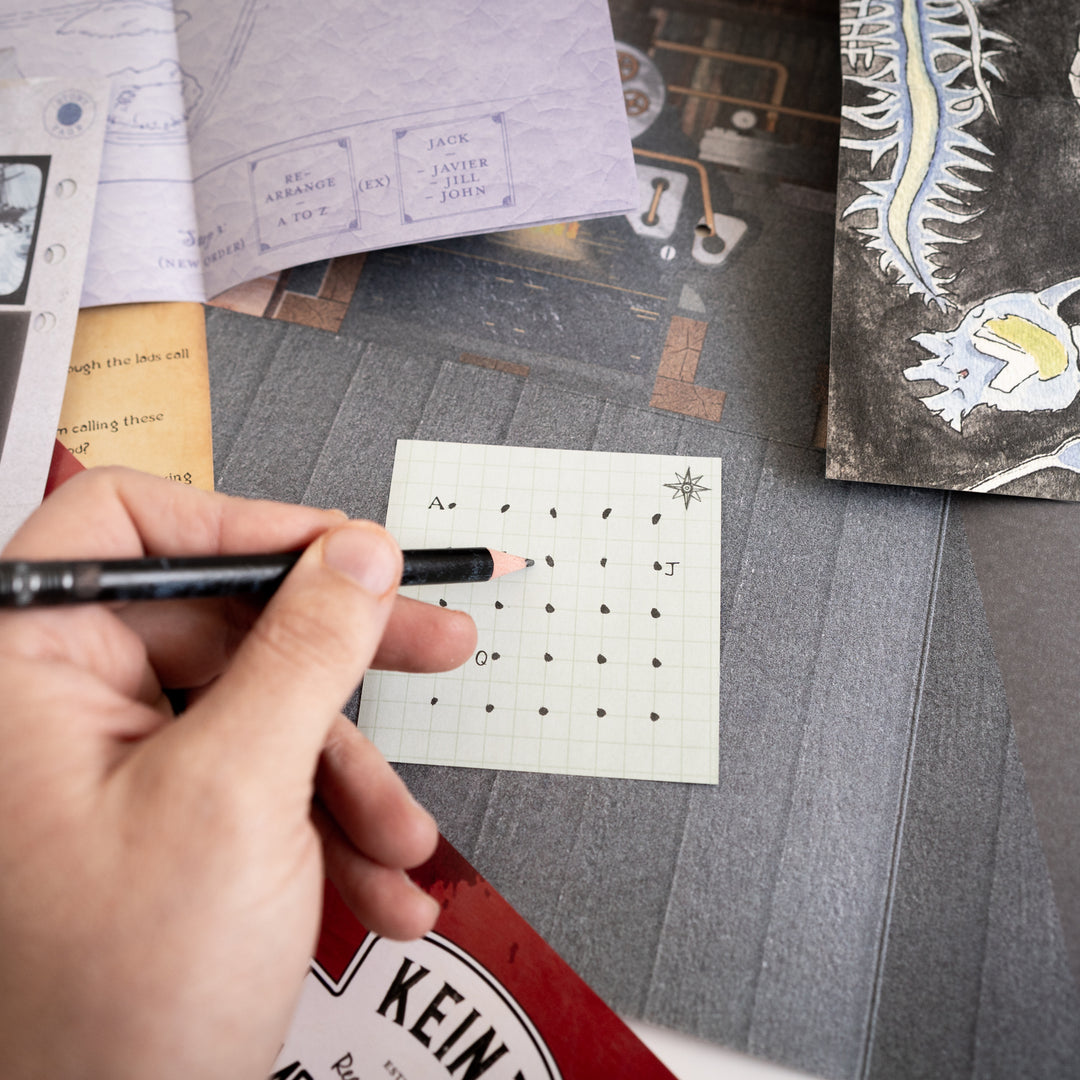 Hand holding a pen over a small sheet of paper with connect the dot patterns on a textured surface. Games Night in an envelope and tabletop Escape Room Game. Similar to an Exit Game. Same genre as murder mystery.