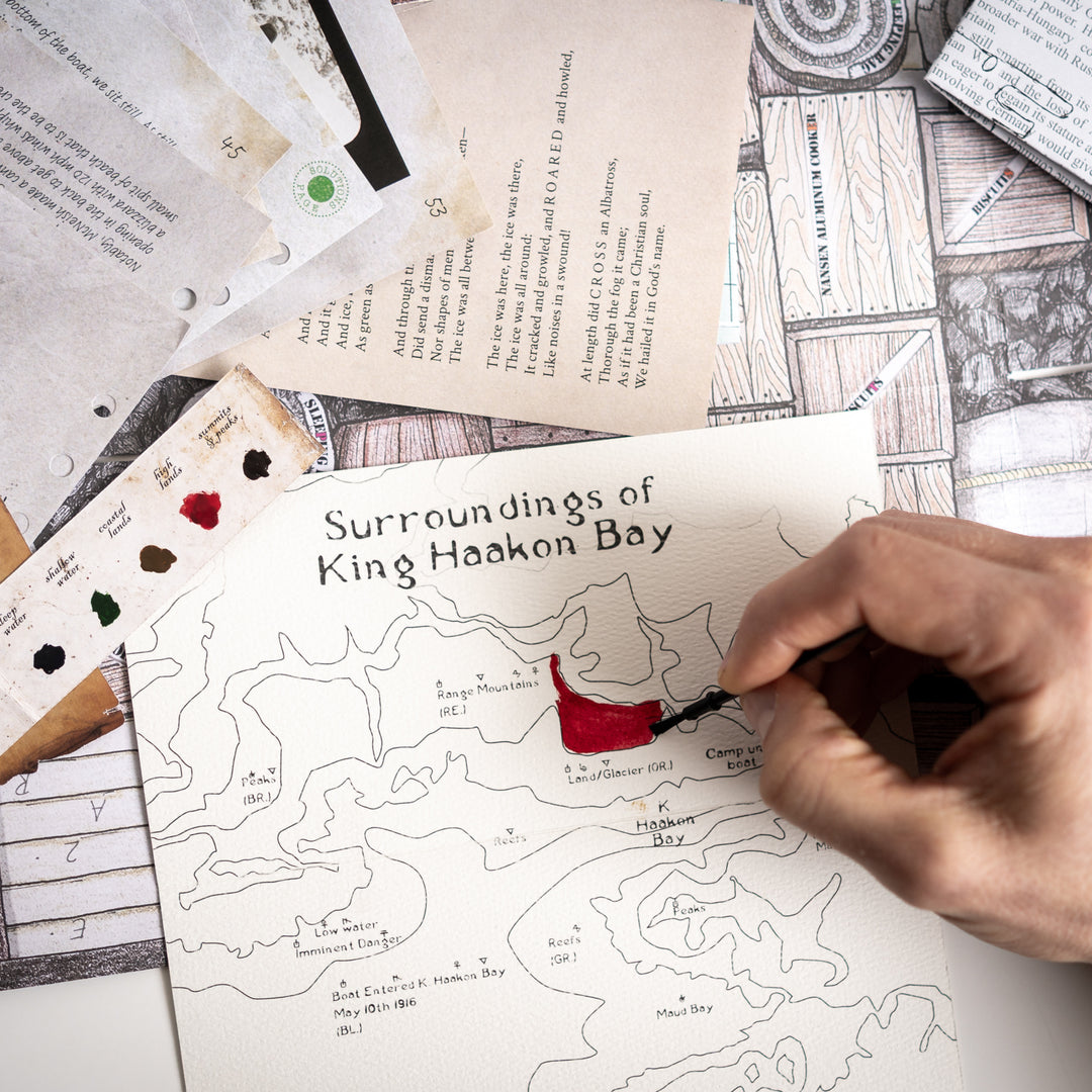 Hand coloring a map of King Haakon Bay with a red paint on a table with other maps and materials. Games Night in an envelope and tabletop Escape Room Game. Similar to an Exit Game. Same genre as murder mystery.