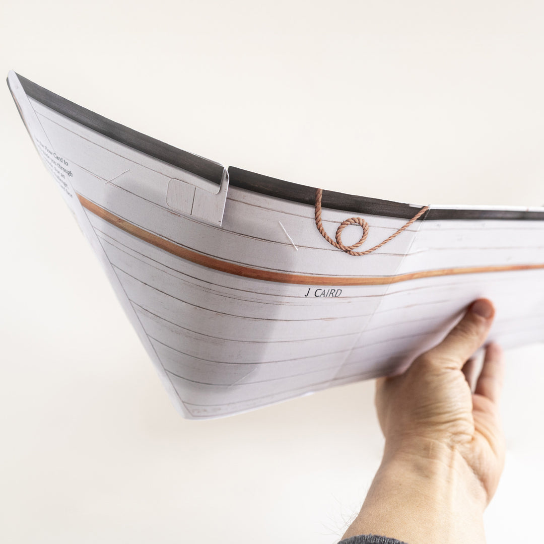 Hand holding a James Caird replica boat made of an envelope from The Shackleton Series. Games Night in an envelope and tabletop Escape Room Game. Similar to an Exit Game. Same genre as murder mystery.